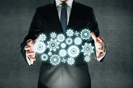 Team work concept with businessman in suit holding abstract gears on dark concrete backgroundの写真素材