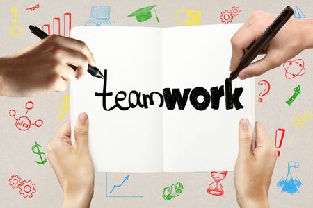 Teamwork concept with hands holding and writing in notepad together on concrete background with colorful business sketchesの写真素材
