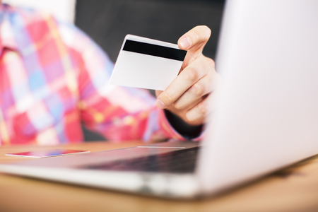 Closeup of blurry man hand holding credit card over laptop keyboard. Online shopping conceptの写真素材