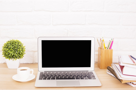 Closeup of creative hipster desktop with blank laptop, coffee cup and other stationery and decorative items on white brick  background. Mock upの写真素材