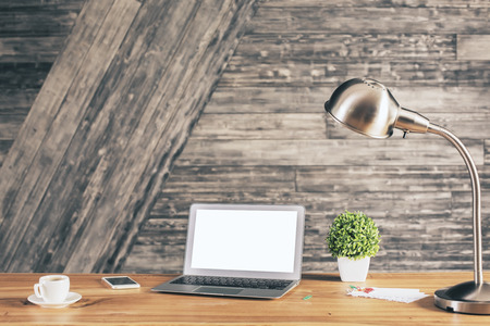Front view of creative designer desktop with blank white laptop, coffee cup, smartphone, plant, some stationery items and table lamp. Mock upの写真素材