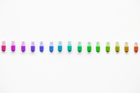 Straight row of colorful rainbow capsules on white backgroundの写真素材