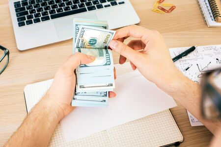 Top view of man counting money above wooden office desktop with various items. Bribery and corruption conceptの写真素材