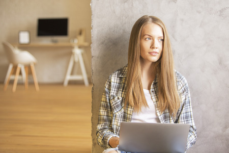 Attractive woman with laptop sitting on floor against concrete wall in officeの写真素材
