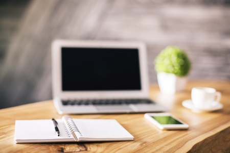 Front view of wooden designer workplace with blurry blank laptop, stationery items, coffee cup, cell phone and plant. Selective focus. Mock upの写真素材
