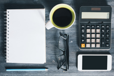 Top view of wooden office desktop with blank mobile phone, spiral notepad, coffee mug, glasses, blue pencil and calculator. Closeup, Mock upの写真素材