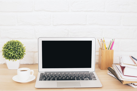 Creative designer desktop with blank laptop, coffee cup, stationery items and plant on white brick wall background. Mock upの写真素材