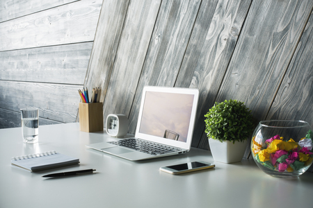 Side view of creative designer workspace with laptop, smartphone, stationery items, clock, water glass and other objects on wooden plank background. Mock upの写真素材
