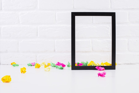 Empty see-through picture frame and colorful crumpled paper pieces on white brick background. Mock upの写真素材
