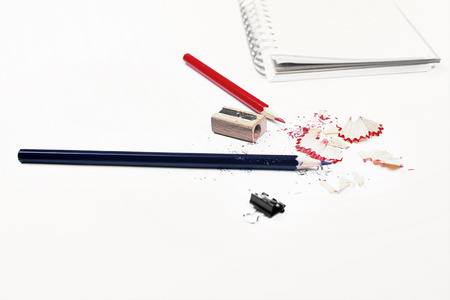 Closeup of white desktop with pencils, sharpener, sawdust, small peg and spiral notepad