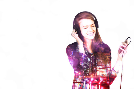 Happy casual girl listening to music on light background with night city view. Double exposureの写真素材