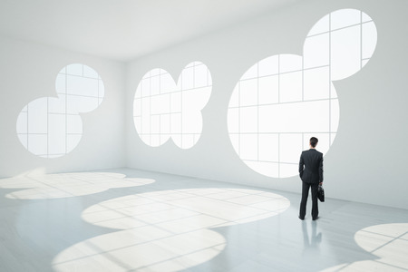 Thoughtful businessman in abstract white interior with round windows, sunlight and shadows. 3D Renderingの写真素材