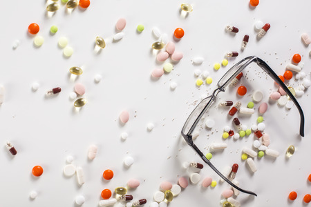 Top view of spectacles and various pills on white backgroundの写真素材