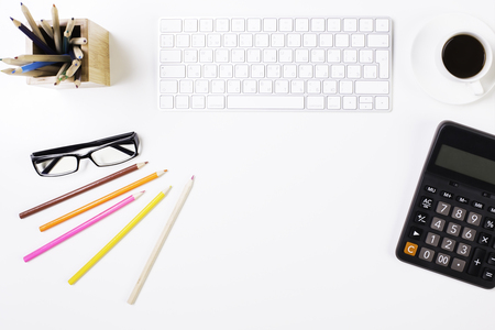 Top view of white office desktop with keyboard, coffee cup, calculator, glasses, stationery items and copy spaceの写真素材