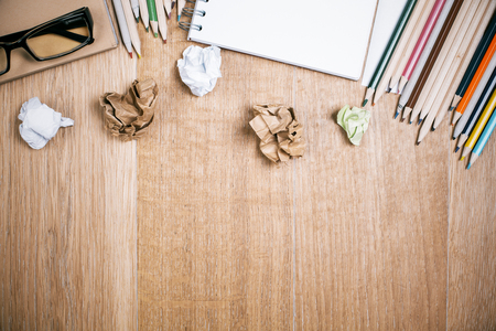 Top view of messy wooden desktop with variety of stationery items, glasses, and crumpled paper balls. Mock upの写真素材