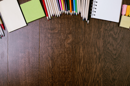 Top view of dark wooden office desktop with colorful pencils, stickers, notepads, paper sheets and other items. Mock upの写真素材