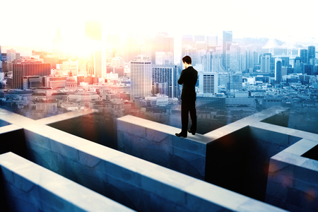 Businessman on top of concrete maze wall thinking on city background with sunlightの写真素材