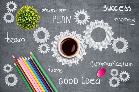 Closeup of grey wooden desktop with plant, coffee cup, colorful pencils, eraser and multiple cogwheel sketches. Teamwork conceptの写真素材