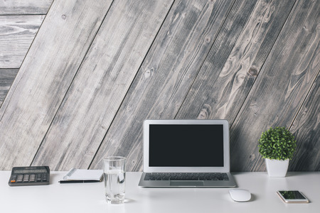 Closeup of creative designer workplace with blank laptop, smartphone, water glass, calculator, plant and other items on wooden plank background. Mock upの写真素材