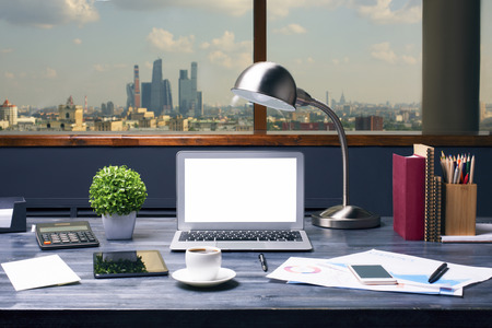 Creative designer desktop with blank white laptop computer, table lamp, plant, coffee cup, tablet, cellphone, calculator, business report, stationery and other items on city background. Mock upの写真素材