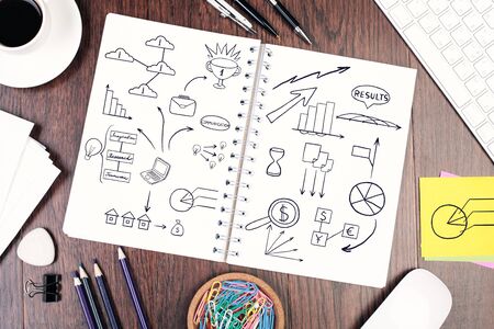Top view of spiral notepad with business sketch on wooden desktop with coffee cup, supplies and...