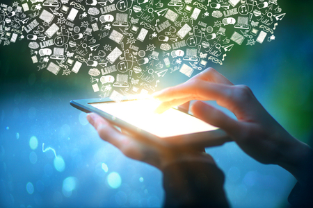 Closeup of male hands holding and touching illuminated screen of digital tablet with abstract communication icons on blue background. Social media concept