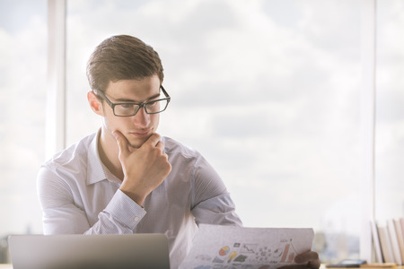 Young businessman in glasses reading documentation in bright officeの写真素材