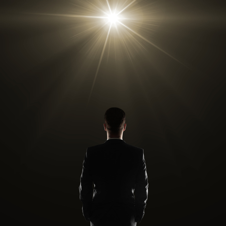 Back view of young businessman in suit on dark background illuminated with a lamp. Research conceptの写真素材
