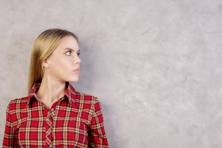 Side view of pretty european woman in red shirt on textured concrete wall background with copy spaceの写真素材