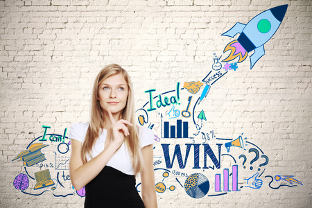 Attractive thoughtful businesswoman standing against brick wall with creative space ship sketch. Startup conceptの写真素材
