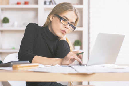 Portrait of beautiful caucasian businesslady using laptop computer at office desk with paperwork and other objectsの写真素材