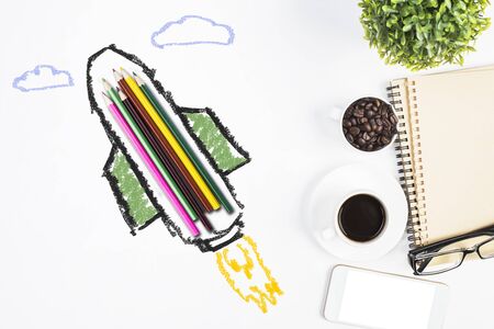 Abstract rocket ship sketch around colorful pencils on white desktop with coffee cup, glasses, smartphone and other items. Education conceptの写真素材