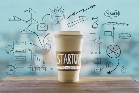 Startup concept with take away coffee cup and abstract business drawings on wooden desktop and blurry city view backgroundの写真素材