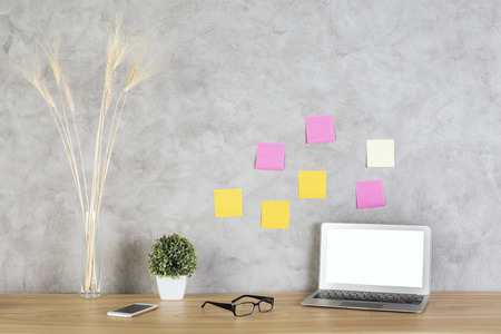 Front view of white laptop on wooden desktop with glasses, smartphone and decorative plants on...