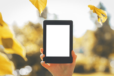 Closeup of woman's hand holding white pad on bright background with autumn leaves. Mock upの写真素材