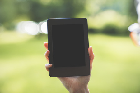 Female hand holding tablet on blurry green landscape background. Mock up