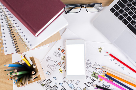 Top view and close up of office workplace with blank white mobile phone, creative business sketches, colorful pencils, notepads, keyboard and other items. Mock upの写真素材