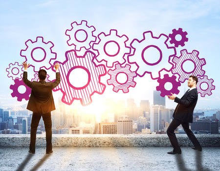 Young businessmen in suits holding abstract cogwheel sketch on rooftop with city view and sunlight. Teamwork conceptの写真素材