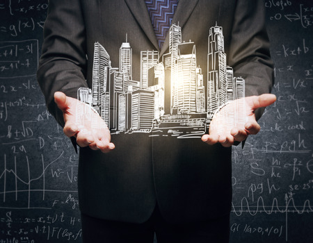 Closeup of businessman's hands holding abstract illuminated city sketch on concrete background with mathematical formulasの写真素材