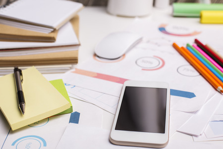 Closeup of office workplace with blank smartphone, financial reports, colorful supplies and other...