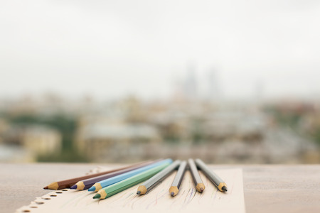 Closeup of colorful pencils on paper sheet placed on wooden windowsill. Blurry city backgroundの写真素材