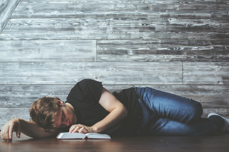 Casual young man with open book sleeping on wooden floor. Tired and overworked concept