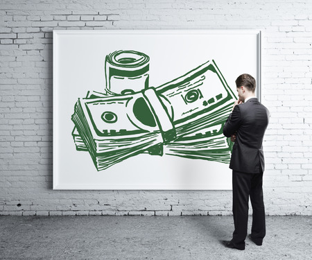 Thoughtful young man looking at whiteboard with creative money sketch in brick room. Money concept. 3D Renderingの写真素材