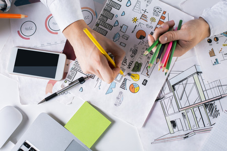 Top view of man's hands drawing creative business sketch with colorful pencils on desktop with blank smartphone and other items. Mock upの写真素材