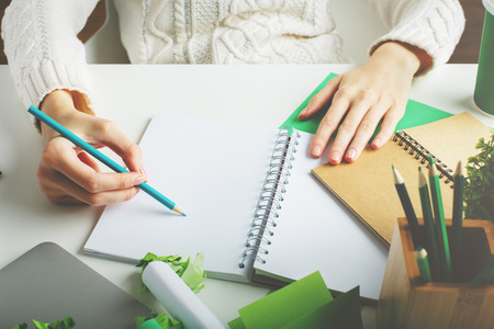 Woman with various creative green items on desktop writing in spiral notepad. Close upの写真素材