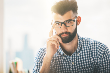 Portrait of casual bearded young businessman in glasses on blurry city backgroundの写真素材