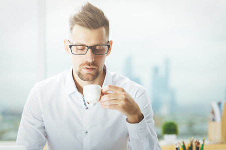 Portrait of handsome caucasian man with coffee cup at workplaceの写真素材