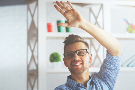 Handsome young businessman at workplace greeting someone with hand waveの写真素材