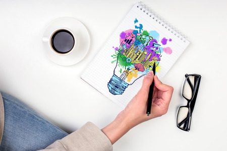 Hand drawing creative sketch in spiral notepad placed on white surface with coffee cup and glasses. Business idea conceptの写真素材