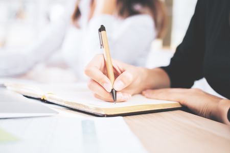 Side view and close up of woman's hands writing in notepadの写真素材